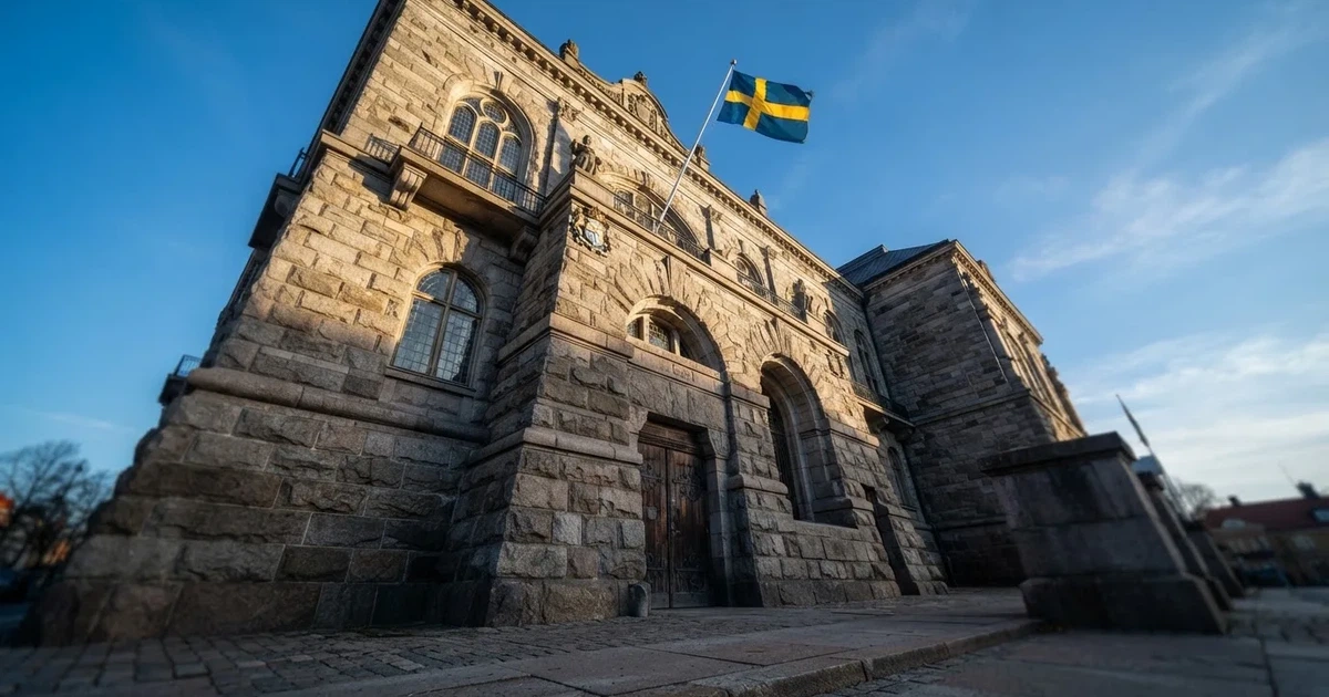 Ett gammalt stadshus i sten fotograferat underifrån mot en klarblå himmel, med den svenska flaggan som fladdrar ovanför entrén.